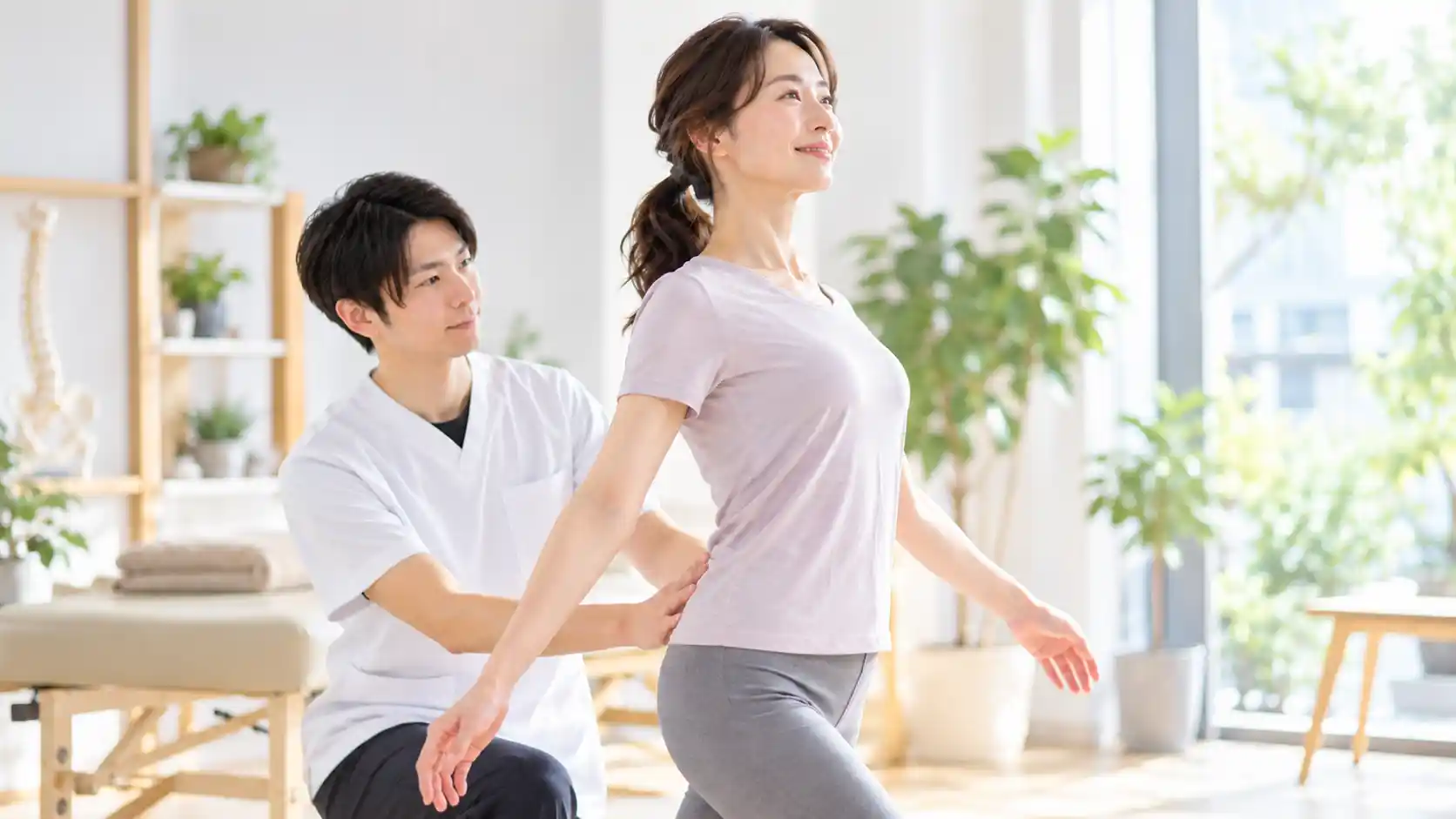 整体院で女性が胸を開き、両腕を後ろに伸ばした姿勢を取り、施術者が腰まわりに手を添えて身体のバランスを確認している様子。